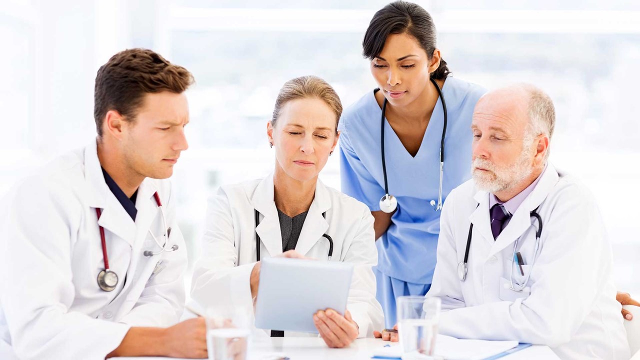 three doctors and a nurse looking at soem data on a tablet