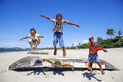 three boys jumping over a boat on a sea shore